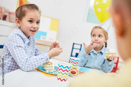Funny kids in birthday cakes eating desserts and cake while having talk by festive table
