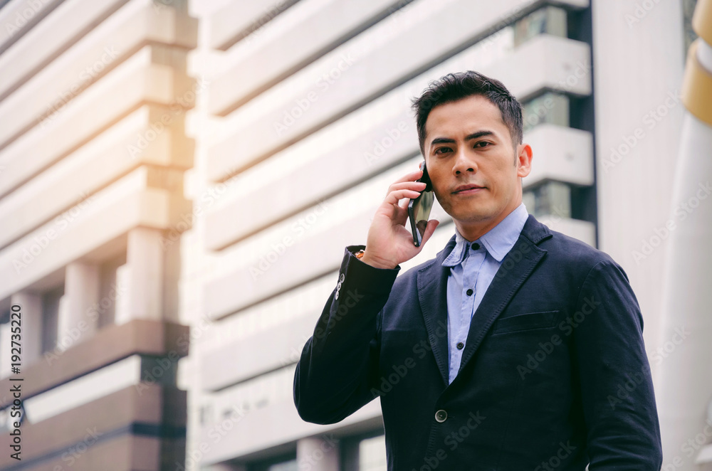 young smart asian business man wearing modern black suit making phone call with mobile smart phone in building city background, internet network connection, technology communication, financial concept young smart asian business man wearing modern black suit making phone call with mobile smart phone in building city background, internet network connection, technology communication, financial concept