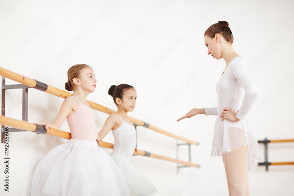 Fototapeta premium Professional ballet teacher talking to one of little ballerinas during training in classroom