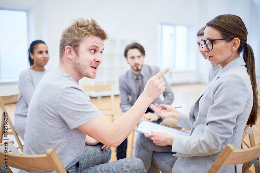 Angry young man pointing at female psychologist during psychological session
