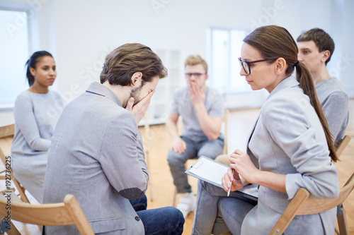 Mature psychologist looking at crying young businessman and trying to give him psychological help during session