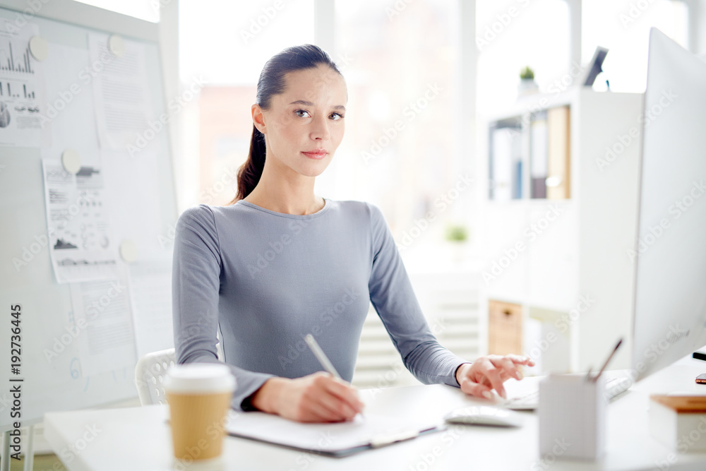 Young pretty manager writing down working points of the day in her notebook