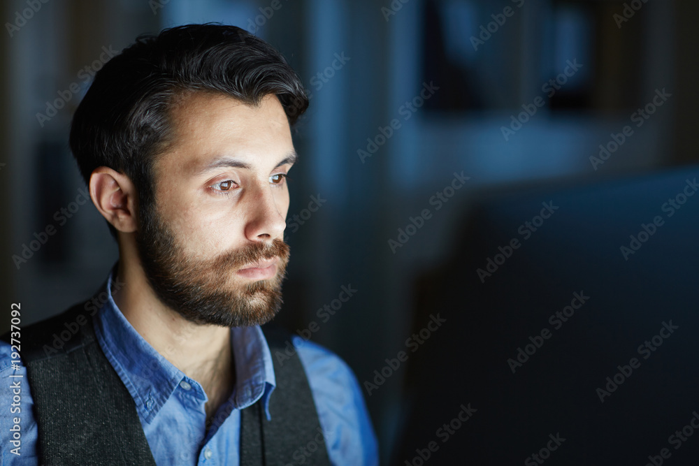 Naklejka premium Serious employee working overtime while sitting in front of computer in the night