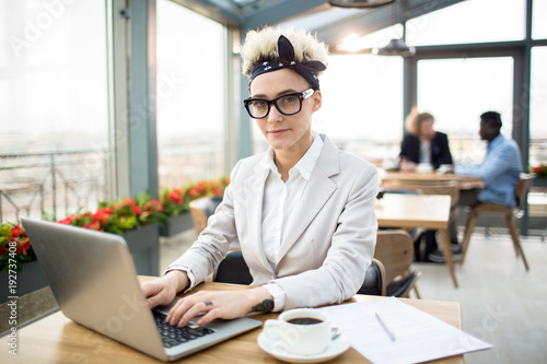 Pretty young blond businesswoman wearing headband, eyeglasses and elegant suit in cafe