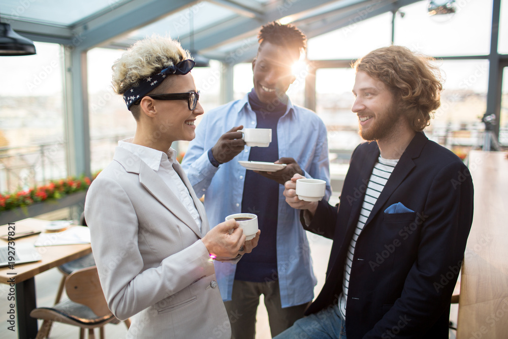 Three restful colleagues having tea or coffee while spending time in cafe by conversation Three restful colleagues having tea or coffee while spending time in cafe by conversation