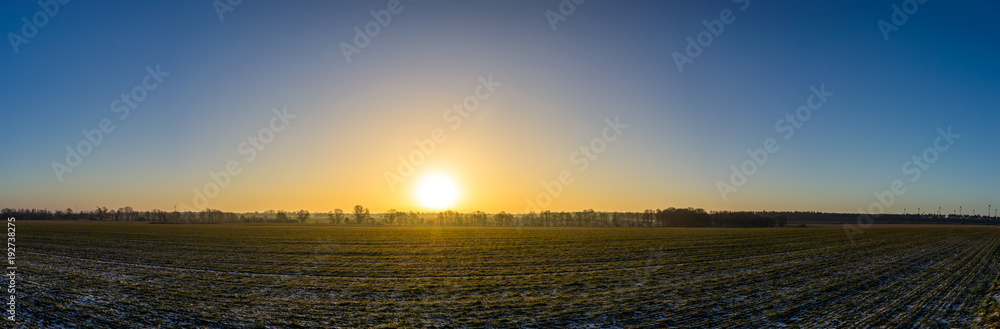 Panorama eines Sonnenaufgangs hinter einem Feld, leicht mit Schnee bedeckt Panorama eines Sonnenaufgangs hinter einem Feld, leicht mit Schnee bedeckt