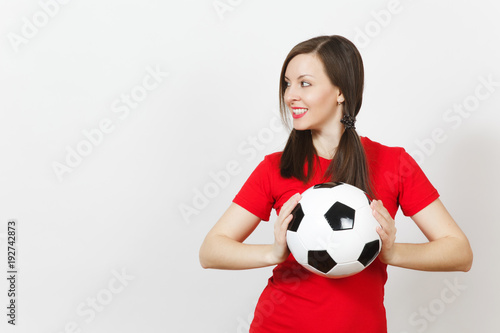 Smiling European young woman, two fun pony tails, football fan or player in red uniform hold classic soccer ball isolated on white background. Sport play football, healthy lifestyle concept. Side view © ViDi Studio