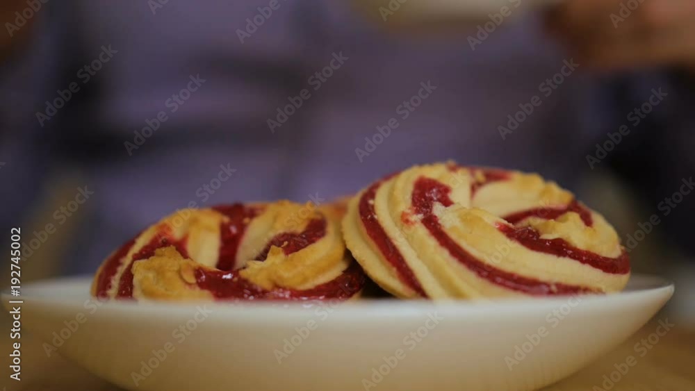 A man is eating a round cookie with jam. Hands taking homemade sweets from the plate. A man is eating a round cookie with jam. Hands taking homemade sweets from the plate.