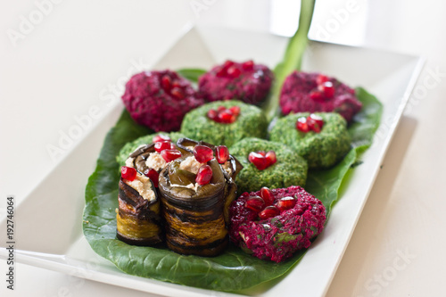 Rolls of eggplant with a filling of walnuts, Georgian snack "pkhali" of spinach and beet with herbs and pomegranate seeds, on a sheet of chard