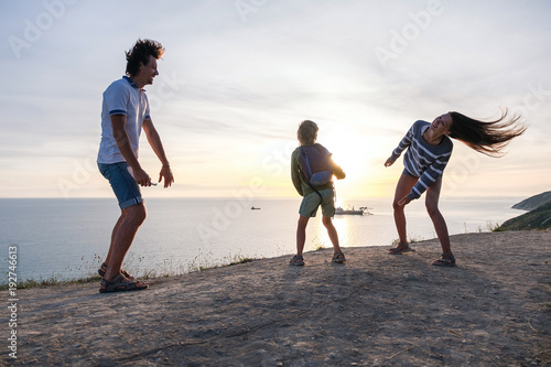 Family fun pastime on a mountain with seaside view. Dad, mom, and son dance together at sunset.