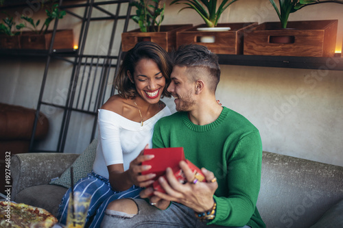 Happy  interracial couple sitting in cafe bar. Man giving gift to his girlfriend.