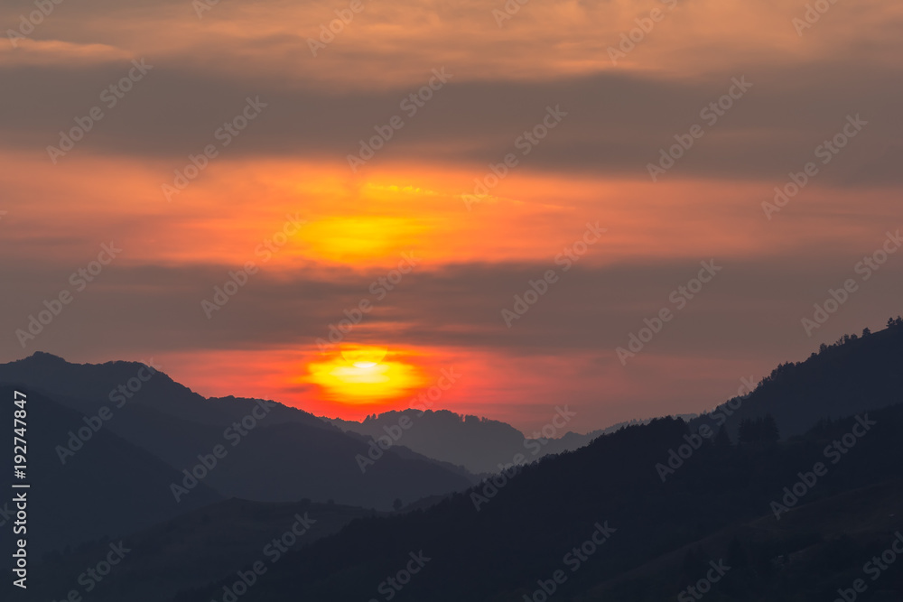 Beautiful landscape of a big setting sun over the silhouette of the mountains, Salciua, Romania