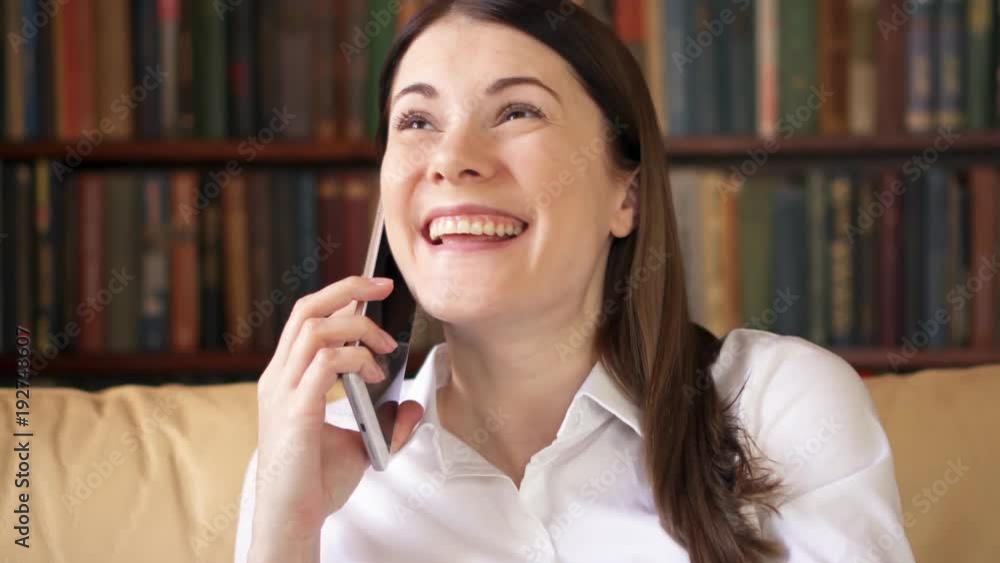 Businesswoman at home talking on smartphone. Young female professional in white shirt recieving good news happy cheerful smiling. Remote freelance work. Success and achievement concept Businesswoman at home talking on smartphone. Young female professional in white shirt recieving good news happy cheerful smiling. Remote freelance work. Success and achievement concept