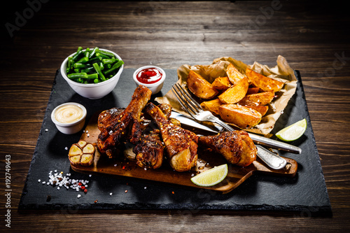 Grilled drumsticks with baked potatoes on wooden background