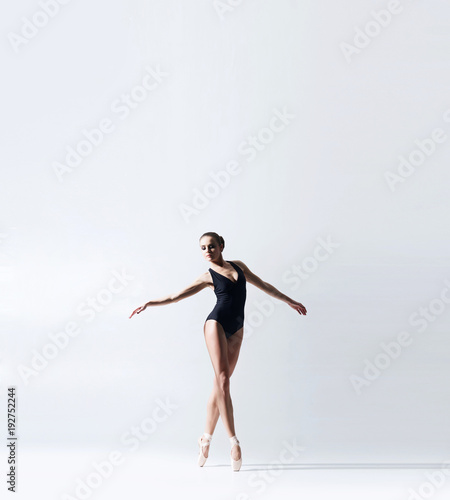 Ballerina in point shoes and bodysuit is dancing in studio. Young and graceful female ballet dancer.