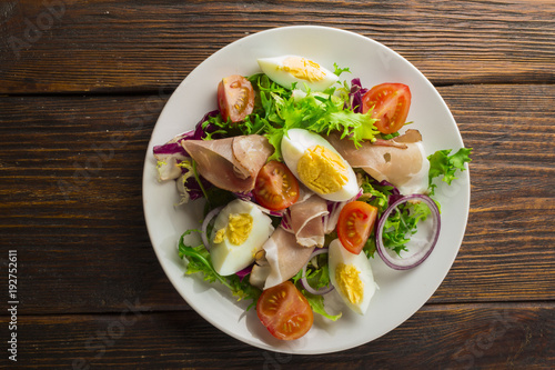 Fresh salad with mixed greens and cherry tomato in bowl on wooden background