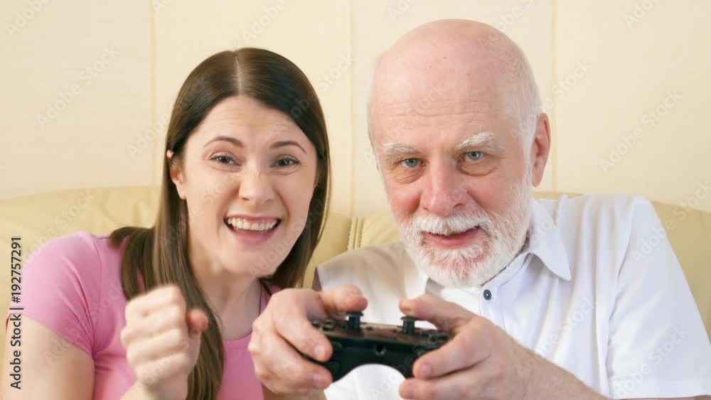 Father and daughter gamers playing video games at home. Addicted senior and teen players with remote controller of game console. Cybersport for active modern elderly people Father and daughter gamers playing video games at home. Addicted senior and teen players with remote controller of game console. Cybersport for active modern elderly people