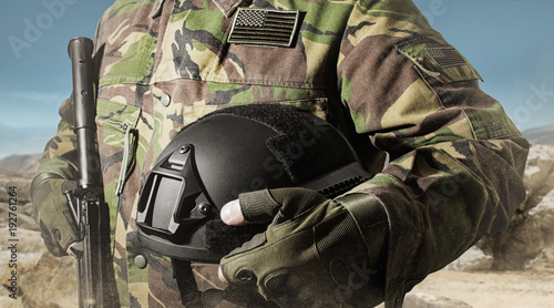 Canvastavla Photo of a soldier in military jacket holding helmet and standing on desert background