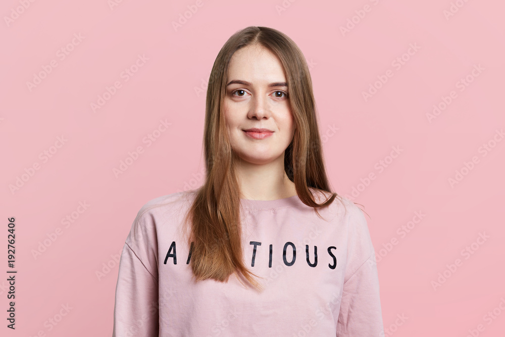 Half length portrait of adorable female model in pink loose sweater, has dark straight hair and pleasant appearance, isolated over pink background. Female student rests alone indoor. Beauty concept Half length portrait of adorable female model in pink loose sweater, has dark straight hair and pleasant appearance, isolated over pink background. Female student rests alone indoor. Beauty concept