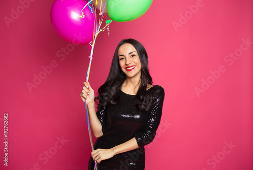 Girl with helium balloons. Beautiful smiling stylish woman in a little black dress with colorful helium balloons on a pink background.