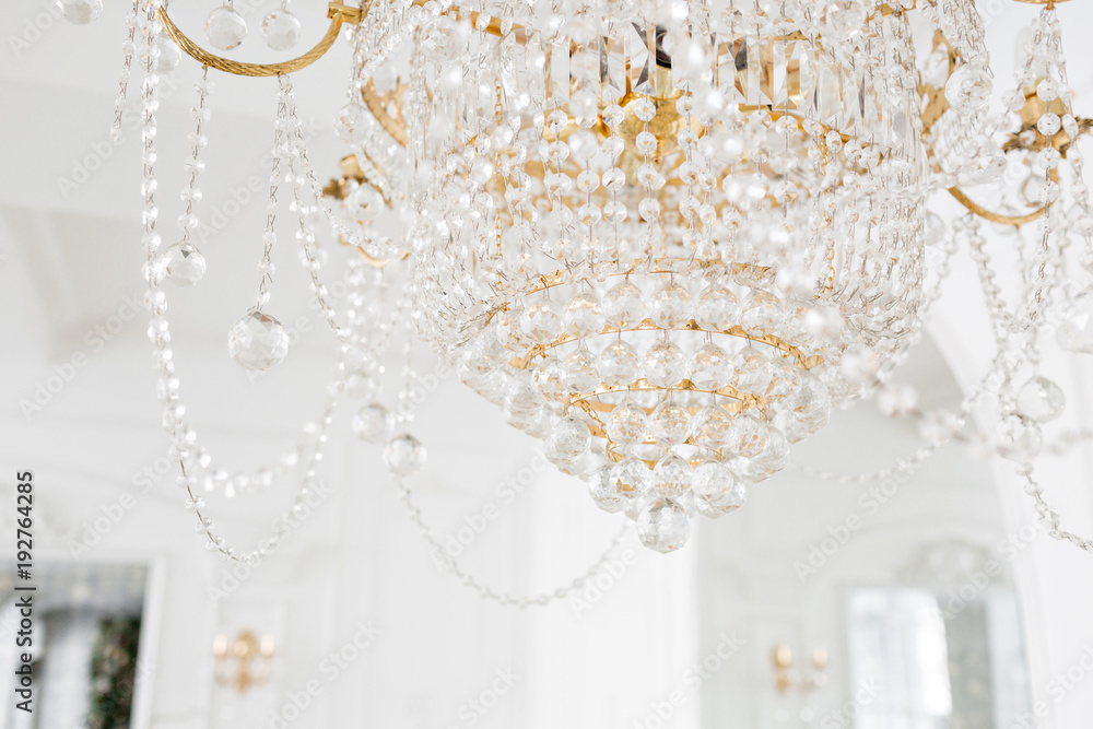 Expensive interior. Large electric chandelier made of transparent glass beads. White ceiling decorated with stucco molding. White patterned. Mouldings element from gypsum.