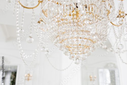 Expensive interior. Large electric chandelier made of transparent glass beads. White ceiling decorated with stucco molding. White patterned. Mouldings element from gypsum.