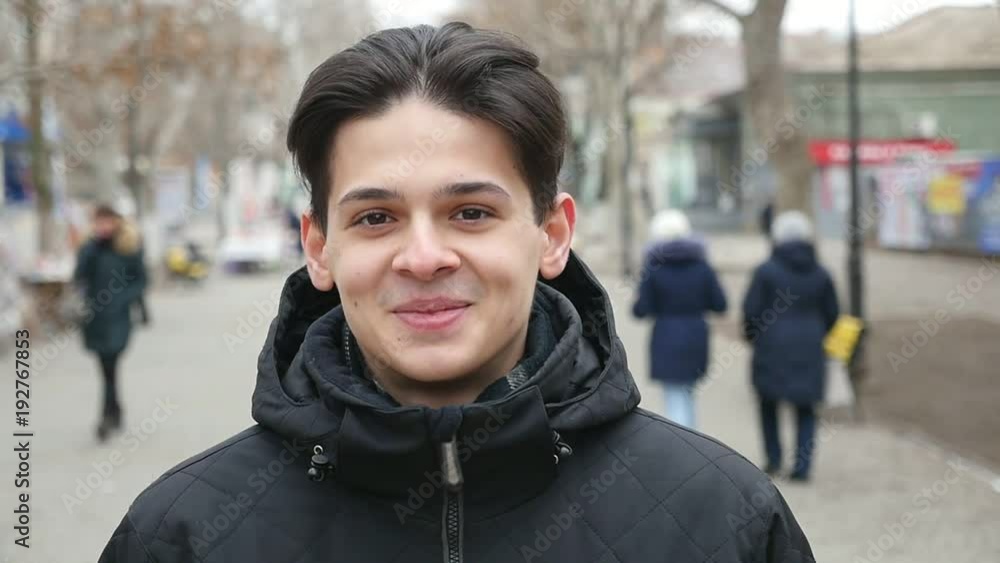 An optimistic view of a stylish young man in a black parka standing in a city street and smiling open-heartedly in winter in slo-mo An optimistic view of a stylish young man in a black parka standing in a city street and smiling open-heartedly in winter in slo-mo
