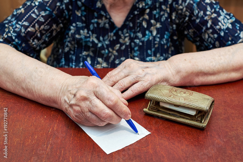 An elderly woman with a purse in her hand writes on blank paper
