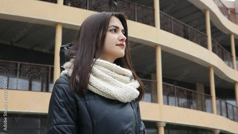 A 180 d. pan shot of a gorgeous girl with long loose hair. She stands in a black parka and white scarf in a street. She waits for her friend A 180 d. pan shot of a gorgeous girl with long loose hair. She stands in a black parka and white scarf in a street. She waits for her friend