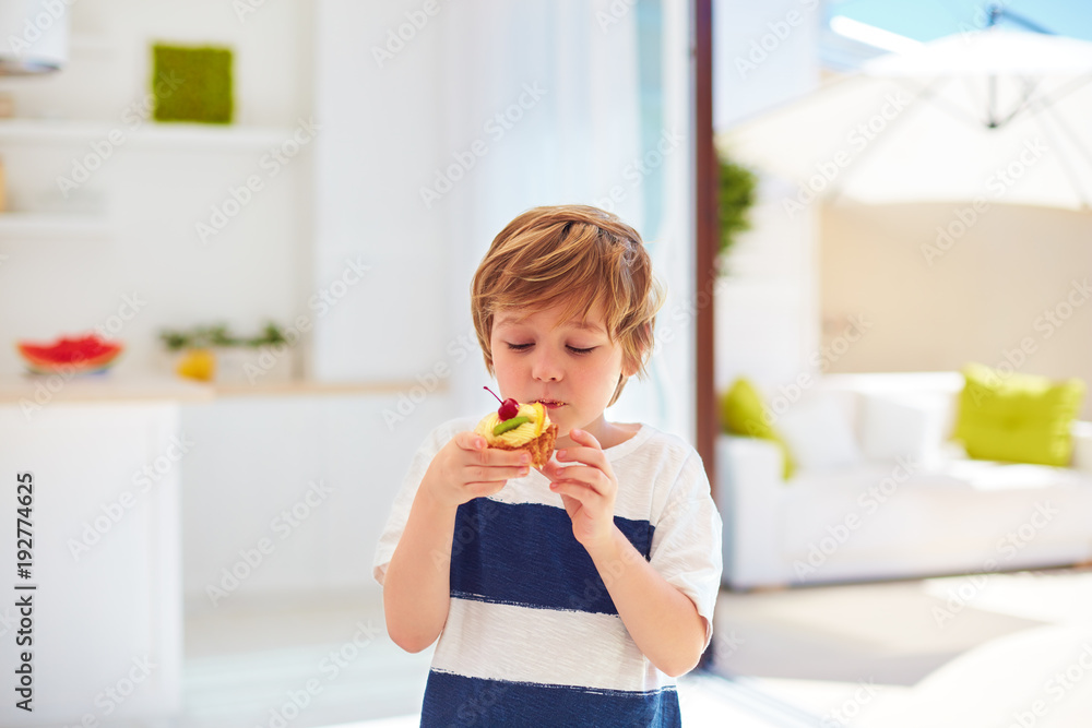 cute kid, young boy eating tasty cupcake with whipped cream and fruits at home cute kid, young boy eating tasty cupcake with whipped cream and fruits at home