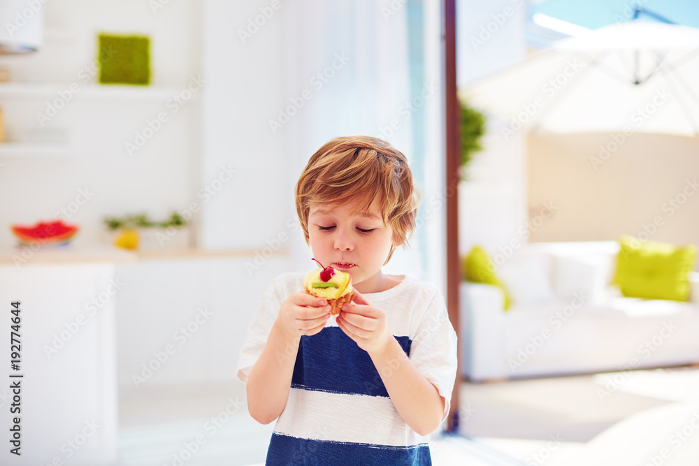 cute kid, young boy eating tasty cupcake with whipped cream and fruits at home cute kid, young boy eating tasty cupcake with whipped cream and fruits at home