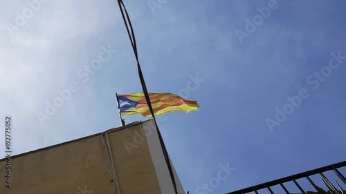 Catalonia red and yellow flag with star waves on building roof under blue sky on sunny day, slow motion photo