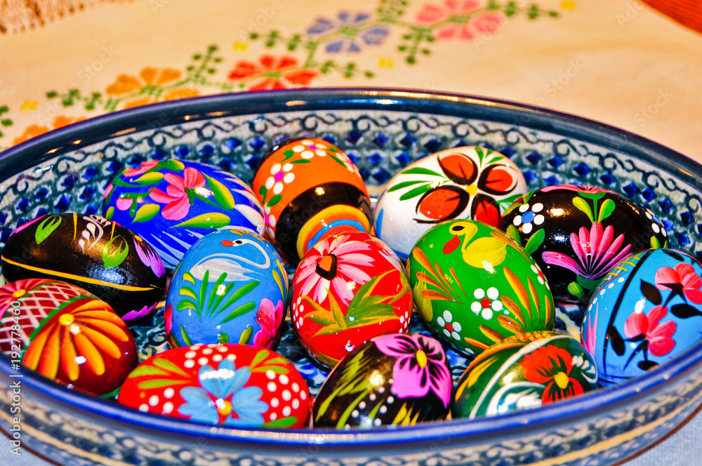 Colorful Hand Painted Wooden Easter Eggs in a Ceramic Bowl on a cloth with a needlepoint flower design.