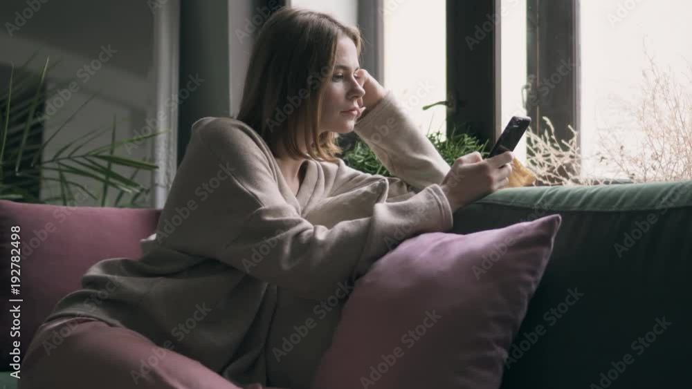 Relaxed woman in sweater using, phone on sofa Relaxed woman in sweater using, phone on sofa