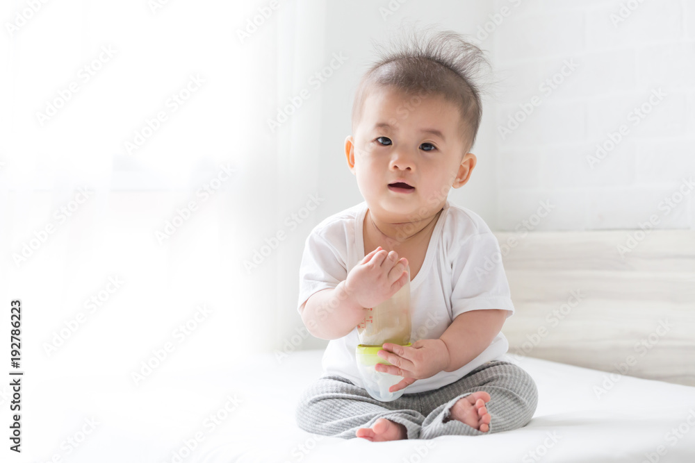 Asian baby boy holding a bottle milk on the bed at home