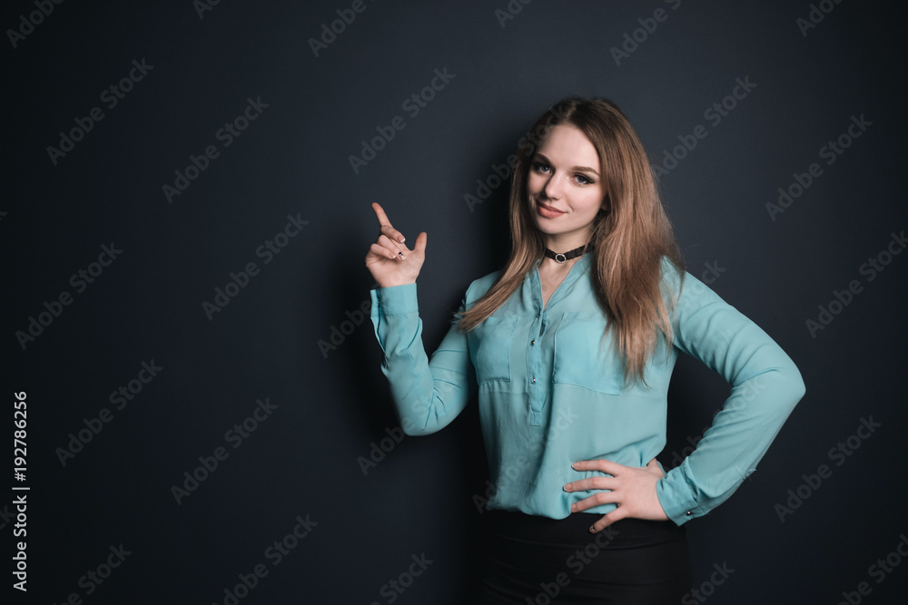 Young girl in blue shirt pointing finger in the free space for text, dark background Young girl in blue shirt pointing finger in the free space for text, dark background