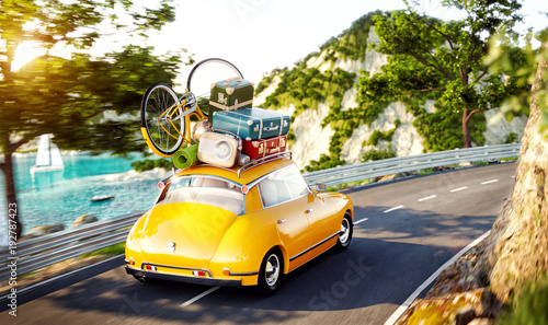Cute little retro car with suitcases and bicycle on top goes by the road alon...