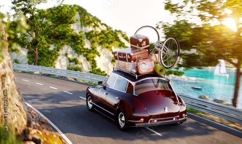 Cute little retro car with suitcases and bicycle on top goes by the road alon...