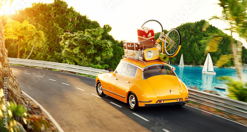 Cute little retro car with suitcases and bicycle on top goes by the road alon...