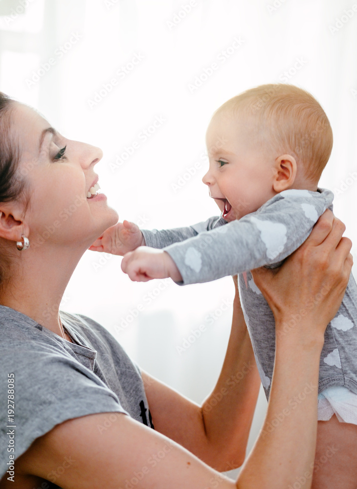 Happy smiling mother and baby playing on bed at home. Happy family having fun. Happy smiling mother and baby playing on bed at home. Happy family having fun.