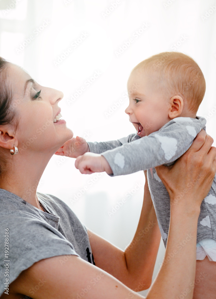 Happy smiling mother and baby playing on bed at home. Happy family having fun. Happy smiling mother and baby playing on bed at home. Happy family having fun.