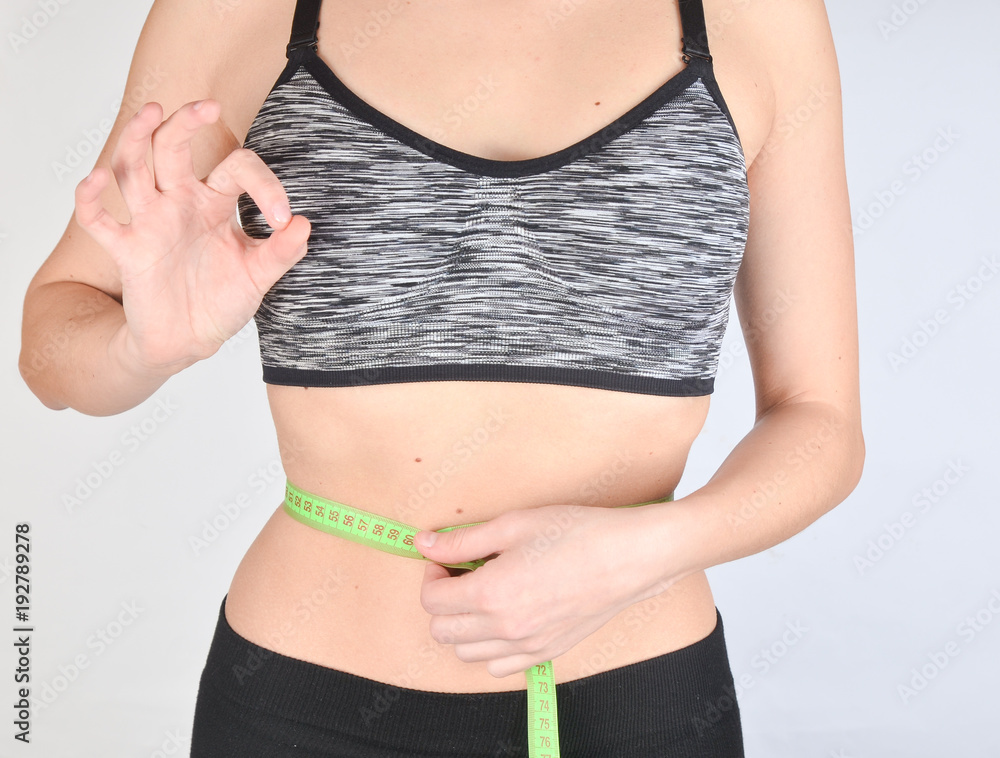 Fototapeta premium Fitness girl in sports tops measuring ruler waist on white background. The concept of losing weight.