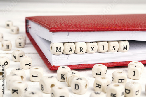 Word Marxism written in wooden blocks in red notebook on white wooden table. photo
