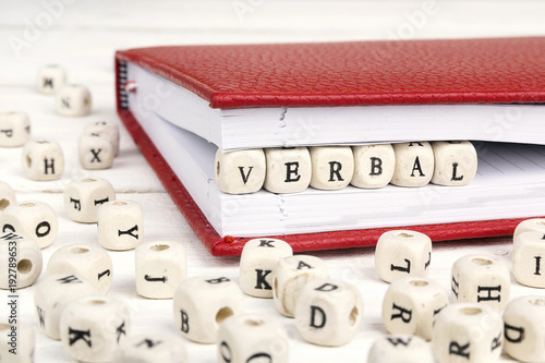 Word Verbal written in wooden blocks in red notebook on white wooden table. photo