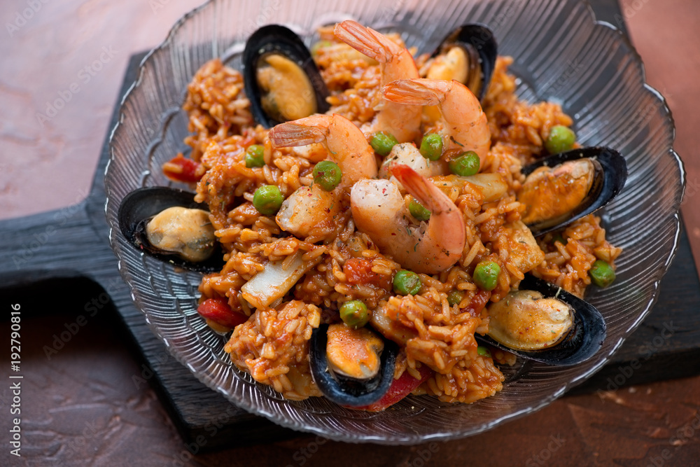 Portion of paella with seafood on a black wooden serving board, selective focus, closeup Portion of paella with seafood on a black wooden serving board, selective focus, closeup