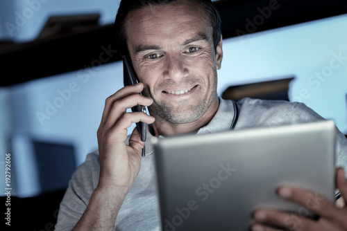 Work is calling. Low angle shot of a positive minded businessman smiling cheerfully while listening to his business partner talking on phone and working on a touchpad.