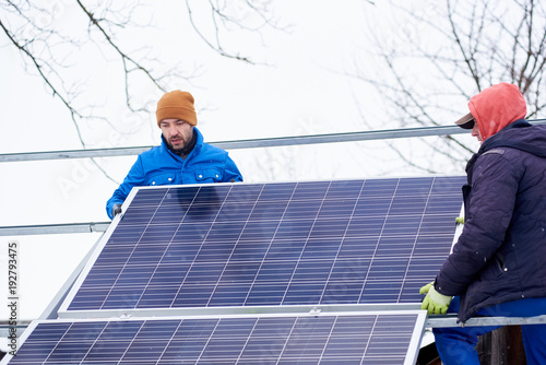 Two workers in the process of installation of the solar battery in winter. Outdoors