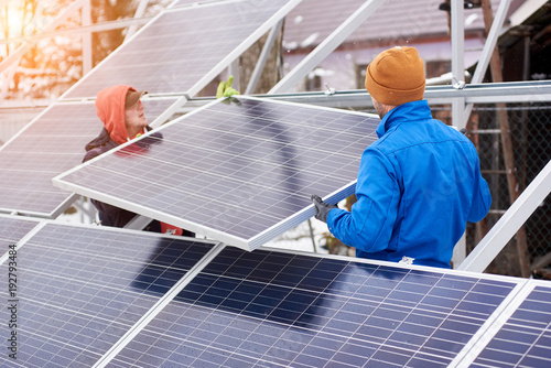 Engineers installing solar panels in winter. Outdoors. Workers are dressed in uniform and warmed with additional clothes photo