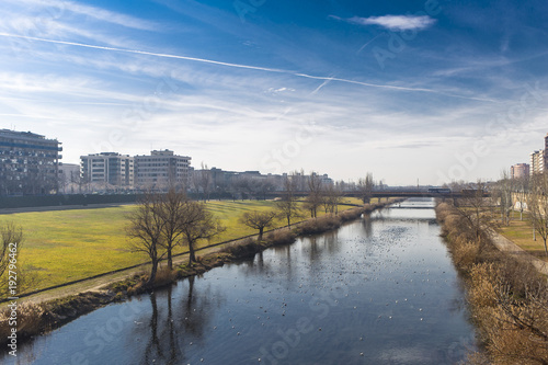 Blue river plain on a green nature park on Lleida city, with architectural details on a the skyline and solid blue sunny sky background