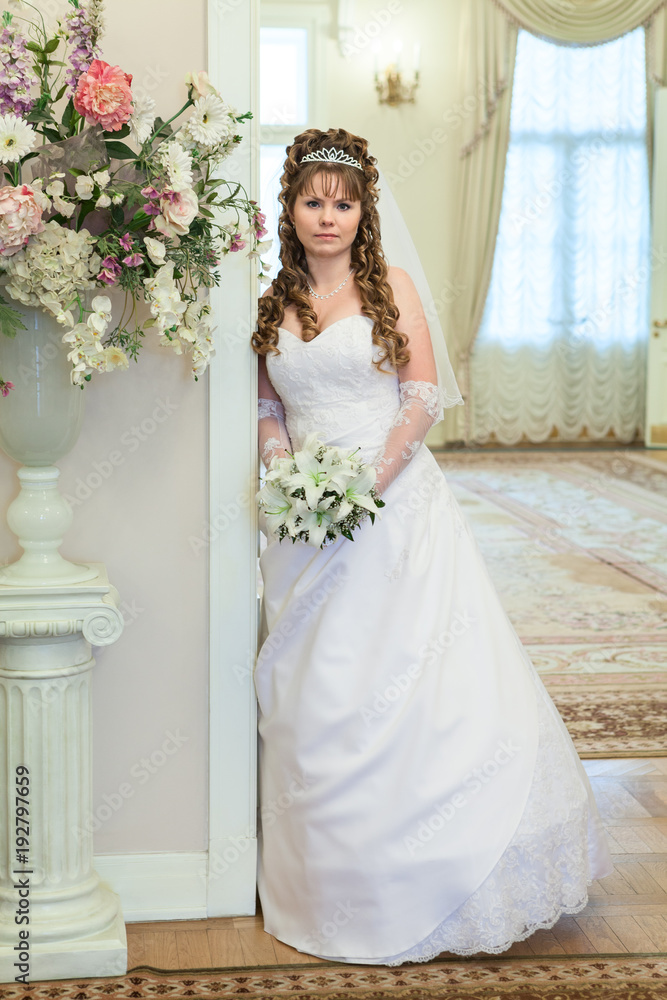 Beautiful young bride standing indoor with wedding bouquet, full-length Beautiful young bride standing indoor with wedding bouquet, full-length